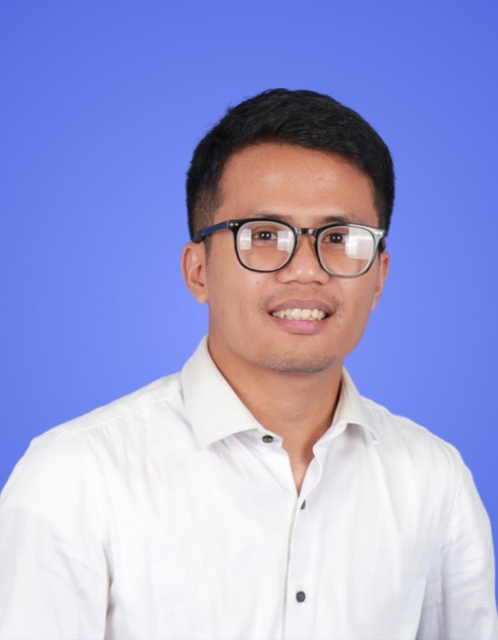 Professional headshot of Handoko wearing a white shirt and glasses with blue background